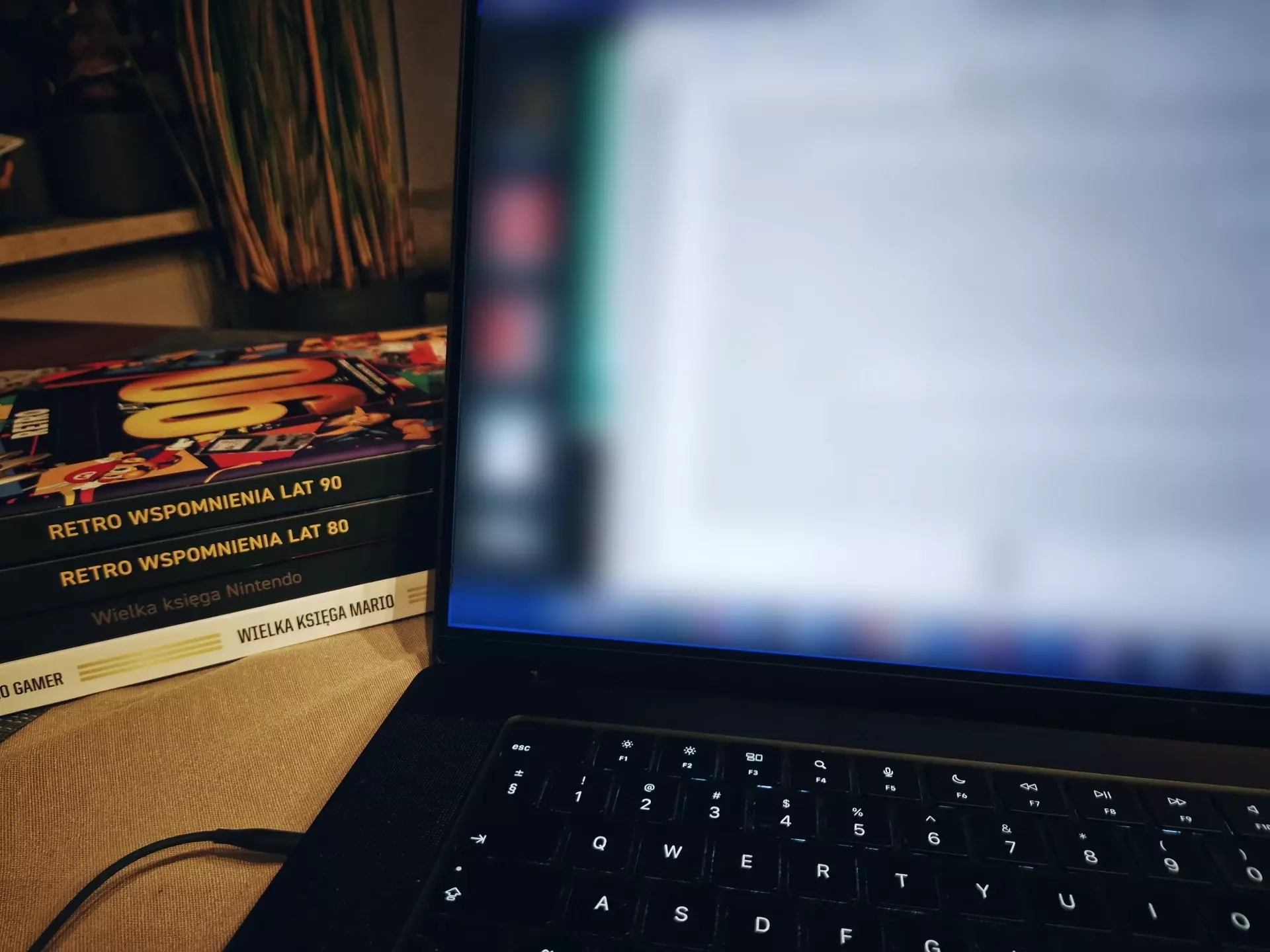 Zdjęcie przedstawiające laptopa z rozmazanym ekranem (tajemnica!), obok którego leżą wcześniejsze książki z wydawnictwa APN: "Wielka księga Mario", "Wielka księga Nintendo", "Retro wspomnienia lat 80" i "Retro wspomnienia lat 90".
